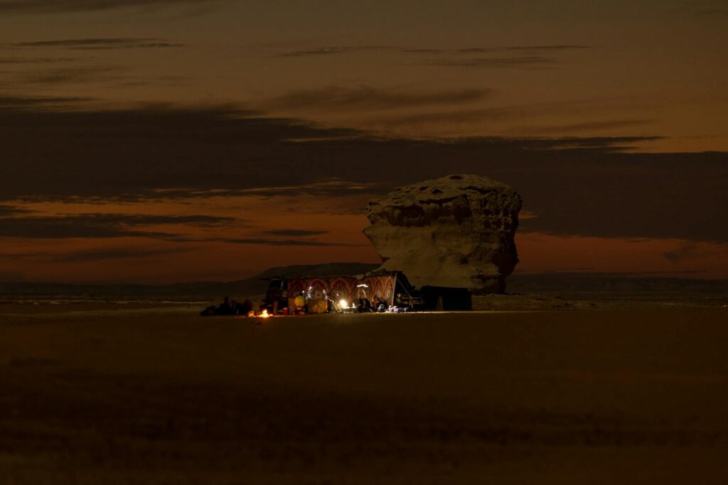 Nighttime campfire in Siwa Oasis, Egypt, with a rock formation and warm desert scenery.