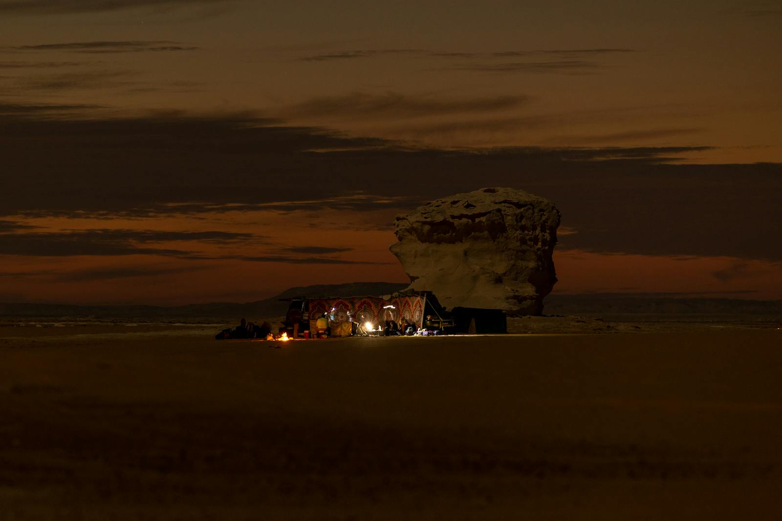 Nighttime campfire in Siwa Oasis, Egypt, with a rock formation and warm desert scenery.
