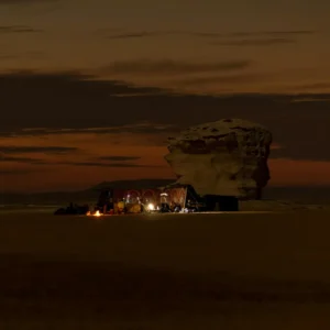 Bedouin camp at night in the Egyptian desert with a campfire and rock formations.