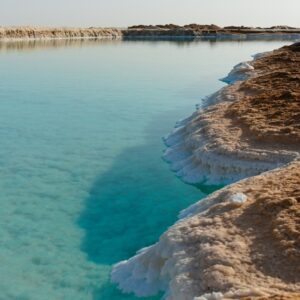 Turquoise water meets salt-encrusted shore under a clear sky.