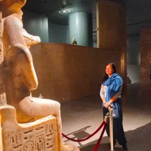 Woman meditating in front of Goddess Sekhmet statue to connect with divine feminine energy in Egypt.