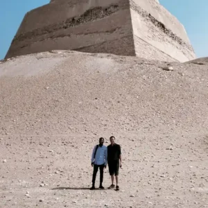 Two travelers standing before the majestic Meidum Pyramid exploring ancient sacred site mysteries