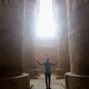 Spiritual traveler touching ancient temple relief to connect with sacred healing energy codes in Egypt.